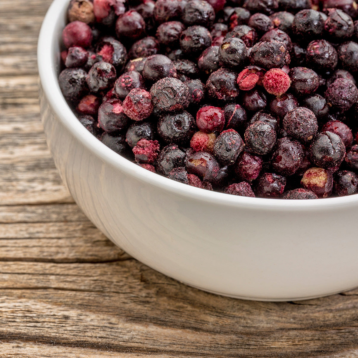 White bowl filled with freeze-dried elderberries on a wooden surface